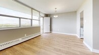 Located at 345 Sentinel Rd in Toronto's York University Heights neighbourhood, this one-bedroom, one-bathroom unit offers a well-organized layout with consistent light hardwood flooring throughout. The open living area is bright and spacious, anchored by large floor-to-ceiling windows along one wall that invite abundant natural light and offer sweeping city views. A pendant light fixture and a glass balcony door further enhance the airy feel of this space. Baseboard heating units run along the windowed walls throughout the unit, ensuring year-round comfort. The kitchen is efficiently designed, featuring white cabinetry with ample storage reaching the ceiling, dark countertops, a subway tile backsplash, and white appliances including a fridge and electric range. The bedroom is a well-proportioned room with its own window for natural light, a built-in double sliding-door closet providing generous storage, and a baseboard heater. The full bathroom is finished in a clean, all-white palette with a full soaker bathtub and tiled surround. Neutral grey-toned walls run throughout the unit, lending a calm, cohesive aesthetic that complements the warm tones of the hardwood-style flooring.