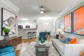 This single-floor residence in Columbus, Georgia offers a thoughtfully designed layout with a warm, contemporary aesthetic throughout. The kitchen features white cabinetry, light stone countertops, black appliances, and a peninsula breakfast bar with seating — seamlessly connecting to the main living area, which is finished with wood-look flooring and neutral tones. A dedicated dining room impresses with crown molding, hardwood-style floors, a modern chandelier, and a bold abstract artwork that anchors the space with color and character. The living room continues the curated feel with soft, neutral walls, decorative crown molding, and carefully placed accent pieces. A cozy reading nook with a leather accent chair adds a functional yet stylish touch. The bedrooms offer plush carpeting, generous natural light from large windows dressed with floor-length drapes, and restful, earthy palettes. The primary bedroom features an elegantly styled headboard and warm ambient lighting. Bathrooms are finished with wood-look flooring, white vanity cabinetry, and clean tile surrounds in the shower-tub combination. A dedicated laundry closet with a full-size washer provides added convenience. The overall ambiance is cohesive, comfortable, and move-in ready.