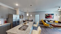 This single-story unit located on Bellaire Boulevard in Richmond, Texas, presents a contemporary open-concept design that connects the kitchen, dining, and living areas into one cohesive, well-lit space. The kitchen is a functional centerpiece, featuring a granite-topped island with an undermount sink, bar seating, gray cabinetry, stainless steel appliances including a refrigerator, range, and microwave, and stylish pendant lighting overhead. Wood-look flooring runs throughout the main living areas, contributing to a clean, modern aesthetic.

Adjacent to the kitchen, the dining area accommodates a round table beneath a statement pendant light, with a direct sightline to the bedroom beyond. The living room offers generous wall space, highlighted by large-scale artwork, and is bright and open in character.

The bedroom is carpeted for comfort, features multiple windows with natural light, crown molding, and ample room for furnishings. The full bathroom includes a granite vanity with gray cabinetry, wood-look flooring, and a tub-shower combination. A dedicated laundry area houses a full-size washer and dryer with overhead wire shelving, adding practical convenience to the unit.