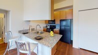 This single-floor unit offers a thoughtfully designed layout with a clear separation between living, sleeping, and utility spaces. The living area features warm hardwood flooring, flush ceiling lighting, and a welcoming atmosphere with ample room for seating and a coffee table. Adjacent to the living space, the kitchen is a functional highlight, equipped with rich wood cabinetry, speckled granite countertops, a breakfast bar peninsula with sink, and black appliances including a refrigerator, range, microwave, and dishwasher. A tile backsplash adds a polished finishing touch.

The bedrooms are carpeted and generously sized, each benefiting from large windows dressed with horizontal blinds that allow natural light to fill the rooms. One bedroom includes a built-in closet, while another features a window with views of the surrounding neighborhood. An electrical panel is conveniently located within one of the rooms.

Two bathrooms serve the unit: one with a granite-topped vanity, large mirror, and shower-tub combo with a decorative curtain, and a second with a clean white soaking tub and shower setup. The overall design is clean and neutral, with white walls throughout creating a bright, open feel that maximizes the sense of space.