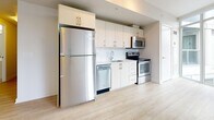 This efficiently designed 1-bedroom, 1-bathroom unit offers a thoughtfully organized layout across a single floor, making excellent use of every square foot. The kitchen is a standout feature, showcasing a full suite of stainless steel appliances — including a refrigerator, electric range, built-in microwave, and dishwasher — paired with crisp white cabinetry, light quartz countertops, a subway tile backsplash, and a stainless steel sink. Light hardwood-style flooring runs throughout the main living areas, contributing to a bright and airy feel. The hallway provides practical built-in storage with sliding panel closet doors, keeping the space organized and uncluttered. The bedroom is a calm, neutral retreat with clean white walls, light flooring, and a dedicated closet. A frosted glass panel in the bedroom allows soft, diffused light to filter through without sacrificing privacy. The bathroom is finished in a clean, all-white palette featuring large floor tiles, a subway-tiled soaking tub and shower combination, a white vanity with under-sink storage, and brushed nickel hardware throughout. The overall aesthetic is modern and minimalist, with a consistent use of light tones and quality finishes that create a cohesive and inviting living environment.
