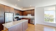 This well-appointed 2-bedroom, 2-bathroom residence offers a thoughtfully designed single-level layout with clean, modern finishes throughout. Light wood flooring flows seamlessly across the entire space, creating a warm and cohesive aesthetic.

The open-concept kitchen is a standout feature, showcasing rich dark wood cabinetry, granite countertops, a central island with additional counter space, and a full suite of stainless steel appliances including a refrigerator, gas range, microwave, and dishwasher. Recessed lighting illuminates the space, which opens directly into the living area for a connected feel.

The living room is bathed in natural light through large windows that frame views of mature trees and the surrounding cityscape. A ceiling fan adds comfort to this airy, sunlit space, which also features access to an outdoor area.

The primary bedroom is generously sized, with large windows and a ceiling fan. Its en-suite bathroom includes a wide vanity with dark wood cabinetry and a large mirror, alongside a walk-in closet with built-in shelving. The second bedroom is bright and well-proportioned, also featuring a window and ceiling fan. The second bathroom offers a full tub-shower combination with white tile surround and matching dark wood cabinetry. Two closets provide ample additional storage throughout the residence.