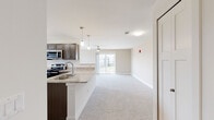 This single-floor residence on W Stoney Creek Dr in Rogers, Arkansas, offers a well-designed open-concept layout that seamlessly connects the kitchen and living areas. The kitchen is outfitted with dark wood cabinetry, light stone-toned countertops, stainless steel appliances including a refrigerator, electric range, and built-in microwave, and wood-look flooring that adds warmth to the space. A peninsula with pendant lighting overhead provides a natural divide between the kitchen and the expansive carpeted living area, which benefits from natural light streaming through a large window and sliding glass doors that open to a private balcony with outdoor views.

The bedroom features plush carpet, a ceiling fan with integrated lighting, a generous window overlooking the surrounding landscape, and a built-in closet with shelving and organizational systems. The bathroom includes wood-look flooring, a natural light source from a window, and clean white fixtures in a simple, functional layout. Throughout the space, neutral tones, white trim, and consistent finishes create a cohesive and inviting atmosphere suited for comfortable everyday living.