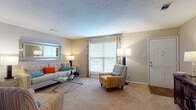 This single-floor 2-bedroom, 2-bathroom residence offers a thoughtfully designed layout across several distinct living areas. The living room is bright and welcoming, featuring plush wall-to-wall carpeting, textured ceilings, and multiple windows dressed with decorative curtains that allow natural light to fill the space. A dedicated dining area provides an elegant setting for entertaining, complete with neutral walls that complement the warm tones throughout. Adjacent to the dining space, a transitional area with hardwood-style flooring leads seamlessly into the kitchen, which is outfitted with white cabinetry, dark granite-style countertops, black appliances including a refrigerator and range, a tile backsplash, and hardwood flooring — creating a functional and stylish cooking environment. Both bedrooms are generously sized with soft carpeting and large windows featuring blinds and curtain panels, offering comfortable retreats with ample natural light. The bathrooms include a tub-shower combination, white vanity cabinetry with granite-style countertops, a large mirror, and hardwood flooring. Throughout the residence, a cohesive neutral color palette, consistent flooring transitions, and well-considered details come together to create a comfortable and inviting living environment.