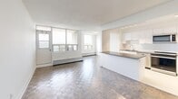 This well-appointed 2-bedroom, 1-bathroom unit offers a thoughtfully designed layout across a single floor. The open-concept living and dining area is generously sized, featuring classic parquet hardwood flooring that adds warmth and character throughout. Large floor-to-ceiling windows flood the space with abundant natural light while framing outdoor views of the surrounding cityscape and greenery, creating a bright and airy ambiance.

The kitchen is seamlessly integrated into the living area via a peninsula counter, offering a functional and social layout. It is finished with white cabinetry, a white subway tile backsplash, dark stone countertops, a stainless steel double sink, and a full suite of stainless steel appliances including a refrigerator, stove, microwave, and dishwasher. Light tile flooring completes the kitchen's clean, modern aesthetic.

Both bedrooms continue the parquet flooring theme and are finished with crisp white walls. The primary bedroom is a comfortable size and benefits from a large window with outdoor views and a baseboard heating unit. The second bedroom is equally bright with clean, neutral finishes.

The bathroom features a full soaker tub and shower combination, accented by white subway tile surround and chrome fixtures, echoing the modern and cohesive design found throughout the unit. A hallway connects all rooms efficiently, completing this functional and stylish home.
