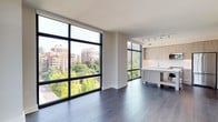 Located on the seventh floor at 4901 Montgomery Lane in Bethesda, Maryland, this contemporary apartment offers a thoughtfully designed open-concept layout bathed in natural light. Expansive floor-to-ceiling windows with bold black steel framing are a defining architectural feature throughout, framing lush treetop canopies and the Bethesda skyline from nearly every room. Dark hardwood flooring flows seamlessly across the living and bedroom areas, providing a rich contrast to the bright, neutral walls and crisp white ceilings.

The open kitchen is outfitted with light wood cabinetry, white quartz countertops, a subway tile backsplash, and a full suite of stainless steel appliances, including a French door refrigerator, electric range, and built-in microwave. A central island adds prep space and a natural focal point connecting the kitchen to the generous living area. Track lighting overhead adds functional illumination to the space.

Bedrooms are well-proportioned, each benefiting from the same dramatic window walls and tranquil outdoor views. The bathrooms are finished with large-format tile flooring and light wood vanities; one features a glass-enclosed walk-in shower, while the other includes a soaking tub. A private curved balcony extends the living space outdoors, offering open-sky views across the Bethesda neighborhood.