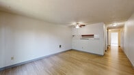 This single-floor unit offers a practical and well-organized layout across several distinct living areas. The main living area features light wood-style flooring, a textured ceiling, and a ceiling fan with integrated lighting. A pass-through shelf connects the living area to the kitchen, enhancing the open flow between the two spaces. Sliding glass doors lead out to a private balcony, offering views of mature trees and greenery, and allowing natural light to fill the room. The galley-style kitchen is efficiently designed with warm wood cabinetry on both sides, white appliances including a refrigerator and electric range, light countertops, and matching wood-style flooring. The bedroom is carpeted for comfort, featuring a window with outdoor views, a wall-mounted heater unit, and a spacious walk-in closet with a rod and shelving. The hallway connects the main areas and includes an additional utility closet housing a water heater with sliding wood-panel doors, as well as a wall heater. The full bathroom is clean and functional, equipped with white cabinetry, a vanity with mirror, and a full-size tub with an overhead shower. Textured ceilings are consistent throughout the unit, contributing to a cohesive, understated aesthetic.