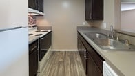 This single-floor unit offers a well-organized layout designed for functional, everyday living. The open-concept living and dining area serves as the heart of the space, featuring a combination of wood-look flooring and plush carpeting that defines each zone. A tiled fireplace anchors one wall of the living area, while large sliding glass doors with vertical blinds provide access to an outdoor space and allow natural light to fill the room. A wall-mounted air conditioning unit provides climate control.

The galley-style kitchen is efficiently designed with dark espresso cabinetry lining both sides, complemented by a mosaic tile backsplash, gray countertops, a stainless steel sink, and a coil-top range. A peninsula with overhead cabinetry separates the kitchen from the living and dining area, providing a natural transition between spaces.

The bedrooms are carpeted and finished in warm neutral tones, each featuring vertical blind-covered windows that bring in natural light. One bedroom includes a sliding closet door. The bathroom is equipped with a tub-shower combination, a toilet, and a dark-cabinetry vanity, all set on wood-look flooring, maintaining a consistent aesthetic throughout the unit.