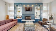 Located in Phoenix, AZ, this sophisticated living room makes a striking first impression with its soaring ceilings and dramatic architectural details. The space is anchored by a stunning accent wall finished in deep teal, housing a classic fireplace with a marble surround, flanked by illuminated mirrored built-in shelving and a wall-mounted television — a refined focal point that draws the eye immediately upon entry.

The flooring throughout is a high-gloss polished concrete with a marbled, metallic finish that reflects light beautifully, contributing to the space's open and airy atmosphere. Tall arched windows line the walls, inviting abundant natural light from multiple directions and offering views of the surrounding greenery.

Elegant archways divide the room into distinct seating zones, creating an inviting and functional flow. One area features chrome-framed leather lounge chairs arranged around a petite side table, while another is anchored by a plush pink sofa and glass-topped coffee table set atop a patterned area rug. A built-in display niche with glass shelving adds a decorative accent along one wall.

The overall ambiance is modern yet warm — a curated blend of contemporary furnishings, reflective surfaces, and classic architectural elements that come together to create a polished and welcoming communal living environment.