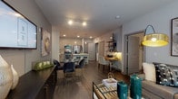 This single-floor residence is designed with a contemporary open-concept layout that seamlessly connects the main living areas. The living room serves as a bright, welcoming centerpiece, featuring wide windows that invite abundant natural light and offer views of surrounding greenery, complemented by wood-style flooring throughout.

The kitchen is well-appointed with stainless steel appliances, including a French door refrigerator, electric range, and built-in microwave. Light wood-tone cabinetry with matte black hardware pairs with white quartz countertops and a subway tile backsplash. A central island with bar seating provides additional workspace and casual dining options, while pendant lighting overhead adds a refined touch.

Adjacent to the kitchen, a dedicated dining area and a built-in desk nook with floating shelves offer functional everyday spaces. The bedrooms feature plush carpeting and large windows with garden views, creating a calm, restful atmosphere. The bathroom is finished with wood-look tile flooring, granite-topped vanity, and a glass-enclosed walk-in shower with white subway tile surround, maintaining the home's clean, modern aesthetic throughout.