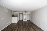 Located at 864 S New Hampshire Ave in the Koreatown neighborhood of Los Angeles, this single-floor unit offers a functional and straightforward layout designed for comfortable urban living. The open living area is finished with light wood-look laminate flooring and neutral gray walls, creating a bright, clean atmosphere. A ceiling fan provides air circulation, while a sliding glass door at the end of the living space invites natural light and offers access to an outdoor area. The galley-style kitchen features white cabinetry, dark countertops, tile flooring, and white appliances including a gas range and microwave, with ample upper and lower cabinet storage on both sides of the corridor layout. A peninsula counter separates the kitchen from the main living area, providing additional workspace. The bedrooms continue the wood-look flooring theme, with neutral walls and textured ceilings throughout. One bedroom features a window dressed with layered curtains that filter natural light warmly into the space. The bathroom includes a full tub-shower combination with a handheld showerhead, tile flooring, and a clean white finish. Textured ceilings are consistent throughout the unit, and white baseboards provide a crisp contrast to the flooring. The overall design is practical and move-in ready, well-suited for those seeking a straightforward residence in a central Los Angeles location.