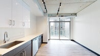 Located in the heart of Portland's South Park Blocks neighborhood, this modern unit at 333 SW Harrison St showcases a compelling blend of industrial and contemporary design. Exposed concrete ceilings with visible ductwork and track lighting run throughout the main living areas, lending an urban loft aesthetic that is both stylish and functional. Light wood-style flooring flows through the open living and kitchen spaces, complementing the clean white walls and dark accent trims.

The kitchen is well-appointed with stainless steel appliances — including a refrigerator, range, microwave, and dishwasher — paired with two-tone cabinetry featuring dark lower cabinets and crisp white upper cabinets, all topped with white countertops. The living area opens to a private balcony through full-height sliding glass doors, framing sweeping views of the Portland cityscape and filling the space with abundant natural light. The bedroom continues the industrial theme with an exposed concrete ceiling, a ceiling fan, plush carpeting, and its own large window with city views. Two bathrooms provide versatility, one featuring a soaking tub and the other a walk-in shower with clean white subway tile. Louvered interior doors and dark-framed entryways add refined, modern character throughout.