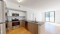 Located along Biscayne Boulevard in Miami, FL, this contemporary single-floor residence offers a clean, modern aesthetic defined by warm hardwood flooring, crisp white walls, and an abundance of natural light throughout. The open-concept layout connects the kitchen and living area seamlessly, creating a spacious and functional flow. The kitchen is well-appointed with stainless steel appliances — including a refrigerator, range, microwave, and dishwasher — complemented by two-tone cabinetry featuring white upper cabinets and warm wood-toned lower cabinets, dark stone countertops, and a subway tile backsplash. A peninsula with a double basin sink and brass faucet adds both style and utility. The living area is bright and airy, benefiting from generous floor-to-ceiling sliding glass doors that open to a private outdoor balcony with views of the surrounding urban landscape. The bedroom is generously sized, featuring a walk-in closet and direct access to the en-suite bathroom, which offers a dual-sink vanity with dark stone countertops and a separate glass-enclosed shower. A second full bathroom includes a soaking tub with tiled surround, a single-sink vanity, and terrazzo-style flooring. The overall ambiance is sleek, light-filled, and move-in ready.