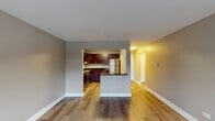 This single-floor residence offers a thoughtfully designed layout that balances open living areas with defined private spaces. The entryway opens through a hallway with hardwood-style flooring, providing views into the main living areas and kitchen beyond.

The open-concept living and dining area features light hardwood-style flooring and neutral warm-gray walls, creating a bright and versatile space. An arched pass-through connects this area to the kitchen, which is well-equipped with rich dark wood cabinetry, dark granite countertops, stainless steel appliances including a refrigerator, range, dishwasher, and microwave, along with an undermount stainless steel sink with under-cabinet lighting.

The bedrooms offer a comfortable retreat, finished with plush wall-to-wall carpeting and neutral tones. Each room benefits from natural light through windows fitted with blinds, and baseboard heating units ensure year-round comfort. At least one bedroom includes a generously sized walk-in closet with built-in shelving and hanging rods.

The bathroom is cleanly finished with light wood-style tile flooring, a dark wood vanity with a white countertop, and grab bars near the shower and toilet area. Throughout the residence, white trim and baseboards provide a crisp contrast against the neutral wall tones, contributing to a clean, cohesive aesthetic.