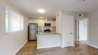 This single-floor unit presents a clean, contemporary design characterized by a neutral color palette, light hardwood-style flooring, and bright white walls that enhance the sense of openness throughout. The open-concept kitchen serves as a central highlight, featuring white shaker-style cabinetry, a subway tile backsplash, and gray quartz countertops. A peninsula with an integrated sink and additional counter space extends into the living area, creating a natural gathering point and clear sightlines across the main living space. Stainless steel appliances — including a gas range, built-in microwave, and refrigerator — complete the kitchen's modern, functional aesthetic.

Natural light enters through windows positioned along the kitchen and living areas, contributing to the unit's airy feel. The bedroom is a well-proportioned, quiet space finished with the same warm flooring and equipped with a ceiling fan for year-round comfort. The bathroom showcases a tub-shower combination elegantly surrounded by large-format marble-look tile in warm neutral tones, accented by brushed nickel fixtures and a recessed niche for added convenience. The overall design is cohesive and move-in ready, blending practicality with refined contemporary finishes.