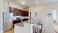 Located at 8891 Moreland St in Powell, Ohio, this single-floor residence offers a thoughtfully designed layout that balances comfort and functionality. The open-concept kitchen is a standout feature, showcasing rich dark wood cabinetry extending to near-ceiling height, granite countertops, a subway tile backsplash, and stainless steel appliances including a range and microwave. A large center island with granite surface provides seating for multiple guests and serves as a natural gathering point. A dedicated walk-in pantry adds generous storage. The kitchen flows seamlessly into a bright living area, where large windows with blinds invite natural light and provide access to an outdoor balcony. The bedrooms are carpeted and serene, each benefiting from natural light through well-sized windows. The primary suite connects directly to a spacious en-suite bathroom featuring a dual-sink vanity with granite countertops, dark wood cabinetry, and hardwood-style flooring. A second bathroom mirrors the same refined finishes. The primary bedroom also includes a walk-in closet with wire shelving. A dedicated laundry room with full-size washer and dryer hookups rounds out the practical amenities. Neutral tones throughout create a calm, cohesive aesthetic across the entire residence.