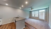 This single-floor residence offers a thoughtfully designed open-concept layout that seamlessly connects the kitchen and living areas. The kitchen is a standout feature, showcasing crisp white shaker cabinetry, a mosaic tile backsplash, stainless steel appliances including a French door refrigerator, electric range, and built-in microwave, all complemented by sleek quartz countertops. A central kitchen island with an undermount sink and additional storage provides both functionality and a natural gathering point. Rich wood-look vinyl plank flooring runs throughout the kitchen and hallway, creating a warm contrast against the neutral gray walls.

The living area transitions seamlessly from the kitchen and is finished with plush carpeting, a ceiling fan with light fixture, and a large window fitted with horizontal blinds that invite ample natural light. The bedroom mirrors this comfortable aesthetic with soft carpet, a ceiling fan, and a generously sized window offering an outdoor view.

The bathroom is clean and functional, featuring a combined tub and shower unit, a quartz-topped vanity with white cabinetry, wood-look flooring, and recessed lighting. A hallway connects all areas efficiently, with multiple doors providing access to closets and additional spaces, completing this well-organized and modern residence.