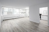 Located at 45 Dunfield Avenue in Toronto's vibrant Midtown neighbourhood, this two-bedroom, one-bathroom unit offers a well-organized layout across a single floor. Light grey laminate wood flooring runs consistently throughout the space, contributing to a clean, cohesive aesthetic.

The living room is one of the unit's standout areas, featuring a wide bank of floor-to-adjacent-ceiling windows fitted with baseboard heating units beneath, allowing natural light to flood the room while framing views of the surrounding Toronto skyline and neighbouring mid-rise buildings.

The kitchen is outfitted with white cabinetry, grey quartz-style countertops, and a stainless steel electric range. A window above the counter provides additional natural light and ventilation. The white tile backsplash adds a crisp, modern touch.

Both bedrooms are well-proportioned, each featuring double-door closets and bright white walls. The primary bedroom is generously sized and benefits from additional windows with city views and baseboard heating. A connecting hallway links the rooms efficiently.

The bathroom features a wide vanity with dual undermount sinks, a taupe quartz countertop, white cabinetry, and a large wall mirror with overhead lighting. The overall design is clean, modern, and functional throughout.