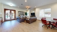 This well-appointed clubhouse in National City, California offers a thoughtfully designed single-floor layout that balances communal gathering with practical functionality. The open-plan kitchen and living area serves as the heart of the space, where warm wood cabinetry, granite countertops, a subway tile backsplash, and stainless steel appliances — including a gas cooktop, wall oven, dishwasher, and refrigerator — create a fully equipped kitchen ideal for hosting. A central island with pendant lighting and bar seating provides an inviting spot for casual dining. An adjoining dining area features glass-top tables and stylish upholstered seating, while the expansive living room accommodates multiple leather sofas, an open shelving unit, and a large flat-screen TV, all set atop light wood-look flooring. Ceiling fans and recessed lighting throughout keep the atmosphere bright and comfortable, and multiple windows dressed with blinds bring in natural light. A dedicated office area offers a generous L-shaped built-in desk, upper cabinetry, and ample workspace. The clubhouse also includes a laundry room for added convenience, making this a versatile and welcoming community facility.