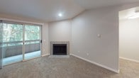 Located at 24420 Russell Rd in Kent, Washington, this single-floor unit offers a well-designed layout complemented by thoughtful finishes and natural surroundings. The living room serves as the heart of the home, featuring vaulted ceilings, plush carpeting, and a tile-surround fireplace that adds warmth and character. A sliding glass door opens to an outdoor area, allowing lush greenery views to pour into the space and creating a seamless indoor-outdoor connection.

The galley-style kitchen is both functional and stylish, appointed with crisp white cabinetry, grey quartz-style countertops, stainless steel appliances including an electric range and refrigerator, and wood-look flooring that extends underfoot. A pass-through connects the kitchen to the living area, enhancing the open feel.

The bedroom is a calm retreat, finished with soft carpet, a window framing verdant tree views, and a baseboard heating system for year-round comfort. A ceiling fan adds to the room's practicality. The hallway connecting the rooms features additional closet space and clean, neutral walls throughout, lending a bright and move-in-ready ambiance to the entire unit. Natural light flows generously through multiple windows, enhancing the welcoming atmosphere of this Kent residence.