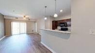 Located at Rivers Pointe Way in Liverpool, NY, this single-floor apartment offers a well-designed open-concept layout that seamlessly connects the main living areas. The entryway opens into a wide hallway with wood-look flooring that extends throughout the main living spaces, creating a cohesive and clean aesthetic.

The kitchen is a standout feature, equipped with rich dark wood cabinetry, granite-style countertops, a full suite of black appliances including a range, microwave, and refrigerator, and a peninsula with pendant lighting that serves as both a functional workspace and a natural divider between the kitchen and living room. The spacious living room is anchored by a ceiling fan with light fixture and offers access to a private patio through sliding glass doors, allowing for natural light and outdoor connectivity.

The bedrooms are carpeted for comfort and include windows that bring in natural light. The primary bedroom connects directly to a bathroom featuring a dark wood vanity with granite countertops, a large mirror, and hardwood-style flooring. Additional rooms provide flexible use of space. Neutral wall tones and clean white trim throughout contribute to a bright, modern, and move-in-ready atmosphere.