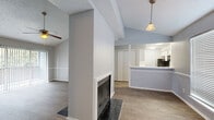 This single-floor, 2-bedroom residence offers a practical and comfortable layout across a well-utilized footprint. The open living area serves as the heart of the home, featuring vaulted ceilings with exposed beams, wood-look flooring, and a standout fireplace with a tiled hearth as the focal point. A pendant light fixture adds warmth to the space, while a large window allows natural light to pour in. The kitchen is positioned adjacent to the living area, separated by a half-wall pass-through counter. It features white cabinetry, ample counter space, a double-basin sink, and black appliances including a range, dishwasher, and refrigerator — all set on light wood-look flooring. The spacious primary bedroom is carpeted and includes a ceiling fan, crown molding, and direct access to an en-suite bathroom. A second bedroom, also carpeted with a ceiling fan and crown molding, features a window for natural light and its own closet. Both bedrooms are served by generously sized walk-in closets with built-in shelving. Throughout the home, neutral gray wall tones and textured ceilings provide a cohesive and understated aesthetic, while the hallway connects the rooms with efficient flow.