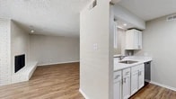 Located in Dallas, TX, this single-story 1-bedroom, 2-bathroom home offers a well-organized layout designed for comfortable everyday living. The living room is a standout space, anchored by a floor-to-ceiling white-painted brick fireplace with a raised hearth and flanked by windows that invite natural light onto the wood-look vinyl plank flooring. Recessed lighting and a textured ceiling add depth to the room's character. The kitchen connects to the living area via a built-in pass-through counter, ideal for casual dining or entertaining. It is outfitted with white cabinetry, white quartz-style countertops, a tile backsplash, stainless steel refrigerator, and a black electric range. The spacious bedroom features plush carpeting, a ceiling fan, a window with natural light, and a generous closet with a rod and shelving. Both bathrooms are clean and functional — one includes a full tub/shower combo with bright white tile surround and chrome fixtures, while the other features wood-look flooring, a white vanity with quartz countertop, and ample upper cabinetry. Neutral warm-gray walls and consistent finishes throughout give the home a cohesive, move-in-ready feel.