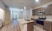 This well-appointed 3-bedroom, 2-bathroom single-floor residence offers a thoughtfully designed open-concept layout. The kitchen serves as the heart of the home, showcasing a large granite-topped island with an undermount sink, rich dark-toned cabinetry, a subway tile backsplash, and a full suite of stainless steel appliances including a range, microwave, and French door refrigerator. Pendant lighting above the island adds a polished finishing touch. The kitchen flows seamlessly into the living area, which features wood-look flooring, a ceiling fan, and access to the exterior through French doors that invite natural light. The bedrooms are carpeted for comfort, each with window blinds and ceiling fans. One bedroom features vaulted ceilings and wood-look flooring, adding an elevated sense of space. The bathrooms are finished with granite vanity tops, dark wood cabinetry, and light tile flooring. A dedicated in-unit laundry closet accommodates a full-size washer and dryer. Throughout the residence, neutral tones, consistent finishes, and thoughtful details create a cohesive, modern living environment.