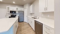 This two-story home offers a thoughtfully designed layout with clean finishes throughout. The kitchen serves as a functional centerpiece, featuring white shaker-style cabinetry, light quartz countertops, a central island, and a full suite of stainless steel appliances including a refrigerator, range, microwave, and dishwasher. Wood-look flooring adds warmth and durability to this space. The main living area is generously sized, with plush carpeting, a ceiling fan, and a staircase leading to the upper level. Multiple bedrooms are spread across both floors, each featuring soft carpeting, neutral-toned walls, and windows that allow natural light to filter in. The upper-level primary bedroom is distinguished by vaulted ceilings and access to a walk-in closet. The bathrooms are finished with white shaker vanities, granite-style countertops, tiled flooring, and tub-shower combinations with bright vanity lighting and large mirrors. Throughout the home, clean white trim, recessed lighting, and a consistent neutral color palette create a cohesive and inviting atmosphere, making this a well-maintained and move-in-ready residence.
