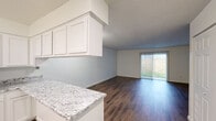 This single-floor residence offers a clean, modern interior designed for comfortable everyday living. The open-concept layout connects the kitchen and living area seamlessly, with a peninsula countertop finished in granite serving as both a functional workspace and a casual dining surface. The kitchen is equipped with white shaker-style cabinetry, stainless steel appliances including a refrigerator and dishwasher, and a textured ceiling that adds subtle character throughout.

Dark hardwood-style flooring flows consistently across the living spaces, complementing the neutral white and soft gray walls. The living area is bright and open, anchored by a sliding glass door fitted with vertical blinds that provide access to an outdoor area with a privacy fence, allowing natural light to fill the room.

The bedrooms are generously proportioned, each featuring the same rich hardwood-style flooring, large windows for natural light, and ample closet space with bifold doors. The bathroom is finished with a granite vanity countertop, white cabinetry, and a well-lit mirror, maintaining the cohesive aesthetic found throughout the residence. Overall, the space presents a fresh, move-in-ready environment with consistent finishes and a practical, functional floor plan.