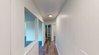 This single-floor residence offers a thoughtfully designed layout with a clean, contemporary aesthetic throughout. A central hallway connects the main living areas, featuring warm wood-style flooring, crisp white walls, and flush-mount lighting that keeps the space bright and welcoming. Unique pass-through window cutouts along the hallway add architectural interest while allowing light to flow between rooms.

The kitchen is well-appointed with slate-gray cabinetry, light countertops, a stainless steel refrigerator, an electric range, and a stainless steel sink — all arranged in an efficient galley-style configuration that maximizes functionality.

The dining area is accented by a stylish multi-light chandelier and continues the wood-style flooring, creating a cohesive feel between the living and dining spaces. Bedrooms are finished with plush carpeting, offering a comfortable contrast to the hard-surface floors elsewhere, and include access to closet space.

The bathroom is clean and functional, featuring a tiled shower-tub combination, a white vanity with a mirror, and wood-look tile flooring. The 3D model reveals a well-organized floor plan with generous room proportions and large windows that invite natural light and outdoor views into the living areas, enhancing the overall sense of openness throughout the home.