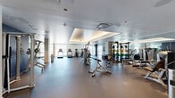 Located at 2059 19th St in Denver, CO, this generously proportioned fitness center offers a comprehensive, well-appointed workout facility spanning a single floor. The space is thoughtfully divided into two distinct zones that together accommodate a full spectrum of exercise modalities.

The main fitness floor features durable rubberized flooring and is lined with an extensive array of strength training equipment, including cable machines, weight racks stocked with colorful bumper plates, benches, and multi-station cable systems. Full-length mirrors amplify the sense of space and allow for proper form checks throughout. Tray ceilings with integrated ambient lighting lend the area a polished, upscale feel, while recessed and flush-mounted ceiling fixtures provide consistent illumination. Large windows along the perimeter invite natural light and frame views of the surrounding Denver skyline, with treadmills and stationary bikes positioned to take advantage of the outlook.

A separate multipurpose studio is outfitted with warm hardwood-style flooring and features a large display screen, functional training accessories including medicine balls, resistance bands, and kettlebells, as well as a rowing machine — making it ideal for group fitness classes, stretching, or personal training sessions. Bold navy accent walls punctuate both areas, complementing the clean white and neutral tones of the overall design. The facility conveys a modern, professional atmosphere throughout.