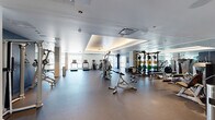 Located at 2059 19th St in Denver, CO, this generously proportioned fitness center offers a comprehensive, well-appointed workout facility spanning a single floor. The space is thoughtfully divided into two distinct zones that together accommodate a full spectrum of exercise modalities.

The main fitness floor features durable rubberized flooring and is lined with an extensive array of strength training equipment, including cable machines, weight racks stocked with colorful bumper plates, benches, and multi-station cable systems. Full-length mirrors amplify the sense of space and allow for proper form checks throughout. Tray ceilings with integrated ambient lighting lend the area a polished, upscale feel, while recessed and flush-mounted ceiling fixtures provide consistent illumination. Large windows along the perimeter invite natural light and frame views of the surrounding Denver skyline, with treadmills and stationary bikes positioned to take advantage of the outlook.

A separate multipurpose studio is outfitted with warm hardwood-style flooring and features a large display screen, functional training accessories including medicine balls, resistance bands, and kettlebells, as well as a rowing machine — making it ideal for group fitness classes, stretching, or personal training sessions. Bold navy accent walls punctuate both areas, complementing the clean white and neutral tones of the overall design. The facility conveys a modern, professional atmosphere throughout.