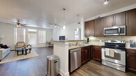 This thoughtfully designed 2-bedroom, 2-bathroom single-floor residence offers a comfortable and functional layout that makes excellent use of its space. The open-concept kitchen and living area serves as the heart of the home, where rich dark wood cabinetry, granite countertops, a peninsula island with pendant lighting, and a full suite of stainless steel appliances — including a dishwasher, range, microwave, and refrigerator — come together seamlessly. A tile backsplash adds a refined detail, while wood-look flooring flows throughout the common areas, creating a warm and cohesive aesthetic. The living room is bright and airy, benefiting from natural light through large windows and a ceiling fan overhead. Both bedrooms are generously proportioned, featuring plush carpet, ceiling fans, and windows with vertical blinds. The primary bedroom is notably spacious and is accompanied by a walk-in closet with built-in shelving. The primary bathroom features a dual-sink vanity with dark wood cabinetry, a tile-surround shower or tub, and matching wood-look tile flooring. A hallway connects the rooms efficiently, and two closets provide ample storage throughout the residence. The overall ambiance is clean, modern, and move-in ready.
