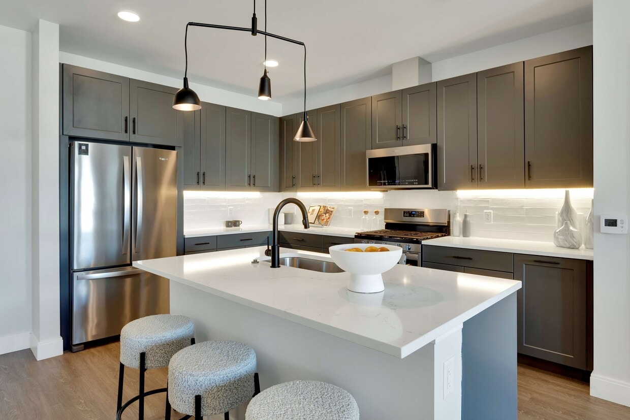 Modern kitchen with sleek dark cabinets, stainless steel appliances, and a stylish island featuring cozy stools and elegant lighting. - The Fitzgerald