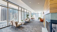 Located in the heart of Chicago's Loop at 210 N Wells Street, this generously sized amenity lounge offers a sophisticated and multifunctional communal space designed to impress. The single-floor layout is anchored by dramatic floor-to-ceiling curtain-wall glazing that wraps around much of the space, flooding the interior with abundant natural light and framing sweeping, unobstructed views of the Chicago skyline.

The living area is thoughtfully divided into distinct zones while maintaining an open, airy feel. A comfortable seating lounge features a plush sofa and accent chairs arranged around soft carpeting with a richly textured, multi-toned pattern that runs throughout. A recreation area houses a sleek white pool table positioned to take full advantage of the panoramic city views. Additional flexible seating vignettes with mid-century modern chairs and cafe-style tables create intimate spaces for conversation or focused work.

A natural wood-clad accent wall serves as a striking architectural focal point, housing a wall-mounted television and adding warmth to the otherwise contemporary palette of white walls and recessed lighting. A fully equipped kitchen with stainless steel appliances, dark cabinetry, and pendant lighting completes the space. Lush indoor plants are positioned throughout, softening the modern aesthetic and enhancing the vibrant, welcoming ambiance of this exceptional urban retreat.