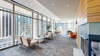 Located in the heart of Chicago's Loop at 210 N Wells Street, this generously sized amenity lounge offers a sophisticated and multifunctional communal space designed to impress. The single-floor layout is anchored by dramatic floor-to-ceiling curtain-wall glazing that wraps around much of the space, flooding the interior with abundant natural light and framing sweeping, unobstructed views of the Chicago skyline.

The living area is thoughtfully divided into distinct zones while maintaining an open, airy feel. A comfortable seating lounge features a plush sofa and accent chairs arranged around soft carpeting with a richly textured, multi-toned pattern that runs throughout. A recreation area houses a sleek white pool table positioned to take full advantage of the panoramic city views. Additional flexible seating vignettes with mid-century modern chairs and cafe-style tables create intimate spaces for conversation or focused work.

A natural wood-clad accent wall serves as a striking architectural focal point, housing a wall-mounted television and adding warmth to the otherwise contemporary palette of white walls and recessed lighting. A fully equipped kitchen with stainless steel appliances, dark cabinetry, and pendant lighting completes the space. Lush indoor plants are positioned throughout, softening the modern aesthetic and enhancing the vibrant, welcoming ambiance of this exceptional urban retreat.