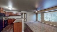 This single-floor residence offers a thoughtfully designed open-concept layout that seamlessly connects the kitchen and living areas. The kitchen is a standout feature, equipped with rich cherry wood cabinetry, granite-style countertops, dark hardwood flooring, and a full suite of black appliances including a range, microwave, refrigerator, and dishwasher. A peninsula counter extends into the living space, providing additional prep area and a natural transition between rooms. The spacious living area is finished with plush carpeting and features a ceiling fan with light fixture. A full-light exterior door leads to an outdoor area, while a large window allows natural light to fill the room. The bedrooms are generously sized, each with soft carpeting, ceiling fans, and ample natural light from well-placed windows. At least one bedroom includes access to a walk-in closet with built-in shelving. The unit includes two full bathrooms: one features a single vanity with granite-style countertop, a mirror, and a tiled floor, while the second offers a matching vanity paired with a full-size soaking tub and shower combination. Throughout the unit, warm neutral tones and consistent finishes create a cohesive and comfortable living environment.