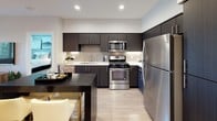 This thoughtfully designed single-floor residence combines modern aesthetics with functional living across several well-appointed spaces. The kitchen is a standout feature, showcasing dark espresso cabinetry that reaches toward the ceiling, white quartz countertops, a classic subway tile backsplash, and a full suite of stainless steel appliances including a gas range, built-in microwave, dishwasher, and refrigerator. A dark-topped kitchen island with bar seating provides additional prep and dining space, while light wood-tone flooring ties the area together seamlessly.

The living room offers a warm, inviting atmosphere with a neutral gray accent wall, an L-shaped sectional sofa, and a sculptural multi-arm floor lamp that adds a contemporary artistic touch. Large windows allow natural light to fill the room, complemented by patterned drapery.

The bedrooms are carpeted for comfort and feature large windows that bring in ample natural light. Each bedroom is generously sized, with room for full furniture arrangements. The primary bedroom includes a distinctive horizontal striped accent wall, adding depth and character to the space.

The bathrooms are finished with dark vanity cabinetry, white countertops, large mirrors, wood-look tile flooring, and shower-tub combinations, maintaining a consistent modern design language found throughout the entire residence.