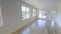 This single-floor space showcases a clean, modern design characterized by an open layout and a bright, airy atmosphere. The main living area is finished with light-toned hardwood flooring that runs throughout, reflecting natural light and contributing to the overall sense of spaciousness. Crisp white walls provide a neutral backdrop that enhances the room's luminosity.

A prominent feature of the space is the generous fenestration along one wall, where two large double-hung windows allow abundant daylight to stream in, offering views of the surrounding greenery and neighborhood streetscape. Adjacent to the windows, a full-lite glass door opens to an outdoor area, further connecting the interior to the exterior environment and adding an additional source of natural light.

Recessed ceiling lighting complements the natural light, ensuring the space remains well-illuminated at all times. White baseboards and window trim add a polished, cohesive finish to the interior. The overall ambiance is fresh and contemporary, making the space feel welcoming and versatile, well-suited for a variety of uses and furnishing arrangements.