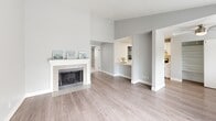 Located at 209 21st Ave SW in Puyallup, WA, this one-bedroom, one-bathroom unit offers a thoughtfully arranged single-floor layout. The open-concept living room is a standout, featuring light hardwood-style flooring, a classic white fireplace with tile surround, and a sliding glass door that opens onto a private balcony with pleasant outdoor views of surrounding greenery. Natural light flows freely throughout the space, enhanced by additional windows fitted with blinds.

The galley-style kitchen is clean and modern, showcasing white shaker cabinetry, light countertops, a stainless steel sink, and stainless steel appliances including a refrigerator and electric range. A pass-through connects the kitchen to the living area, maintaining an open and connected feel. In-unit laundry is also visible within the kitchen corridor.

The bedroom is a comfortable, carpeted retreat finished in soft neutral tones, with a window for natural light and direct access to the bathroom. The full bathroom features wood-look vinyl flooring, a tub/shower combo, and clean white finishes. A dedicated closet and hallway complete the layout, making efficient use of the available space throughout this well-maintained Puyallup residence.
