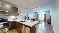 This well-designed single-floor residence offers a thoughtful layout encompassing a combined kitchen and living room, a bedroom, and a closet. The open-concept kitchen is a standout feature, showcasing dark espresso cabinetry, quartz countertops, a tile backsplash, and a full suite of stainless steel appliances including a side-by-side refrigerator, range, microwave, and dishwasher. A peninsula island with an undermount sink provides additional prep space and casual bar seating, illuminated by sleek pendant lighting overhead. Track lighting and recessed fixtures brighten the entire open-concept area. The living room flows naturally from the kitchen and is anchored by wood-look flooring, a ceiling fan, and French doors that invite natural light while providing access to an outdoor area. The bedroom offers plush carpeting, a ceiling fan, and a well-positioned window dressed with blinds and curtain panels that allow for natural light and privacy. Neutral wall tones throughout the residence create a calm, cohesive aesthetic. A dedicated closet provides practical storage. The overall ambiance is modern and inviting, with contemporary finishes and a functional layout designed for comfortable everyday living.
