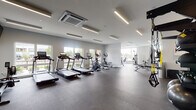 Located at 500 Bank St in New London, Connecticut, this modern fitness center offers a thoughtfully designed workout environment built to support a full range of exercise routines. The space is bathed in natural light, courtesy of large windows that line the perimeter and provide views of the surrounding streetscape and greenery, creating an open and energizing atmosphere.

The facility is equipped with a robust selection of cardio machines, including multiple treadmills and elliptical trainers, arranged along the windowed walls to maximize both light and outdoor sightlines. A dedicated strength training zone features a comprehensive collection of selectorized cable machines, multi-function cable systems, free weights, and adjustable benches, providing options for users at every fitness level.

Underfoot, durable rubber flooring covers the entire workout area, offering safety and comfort during exercise. Full-length wall mirrors amplify the sense of space while allowing users to monitor their form. Overhead, sleek linear LED lighting runs throughout the ceiling, complementing the building's cassette-style HVAC units to ensure a comfortable environment year-round. A mounted flat-screen television keeps members entertained during cardio sessions. A small utility area with cabinetry and a TRX suspension training station rounds out the amenities, making this a well-equipped and versatile fitness facility.