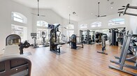 Located at 4630 S Lakeshore Dr in Tempe, Arizona, this fitness center is a single-floor exercise facility designed to support a comprehensive workout experience. The room is defined by its striking vaulted ceilings, which soar dramatically overhead and create a bright, open atmosphere. Large arched windows line the walls, flooding the space with abundant natural light and offering views of the surrounding outdoor environment. Ceiling fans are positioned throughout to maintain airflow and comfort during workouts.

The flooring consists of warm-toned hardwood, lending the space a clean and polished aesthetic. A bold geometric mountain mural in shades of blue and gray serves as a standout accent wall, adding a dynamic visual element to the room's interior design.

The facility is well-stocked with a wide variety of equipment. Strength training is supported by multiple cable and weight machines, a Smith machine, a multi-station functional trainer, and a tiered dumbbell rack with a full range of free weights. Cardio options include several treadmills and stationary bikes. Wall-mounted flat-screen televisions are positioned for easy viewing from multiple areas of the room. A storage cabinet near the accent wall provides space for fitness accessories. The overall ambiance is bright, modern, and motivating, making it a capable and inviting facility for residents.
