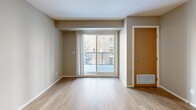 Located in the Skyview Ranch community of Calgary, this two-bedroom, one-bathroom unit offers a functional and well-appointed layout across a single floor. The open-concept kitchen and living area forms the heart of the unit, where light wood-tone flooring runs throughout, creating a clean and cohesive aesthetic. The kitchen is equipped with white cabinetry, dark countertops, and black appliances including a refrigerator, dishwasher, and range, providing ample storage and workspace. A sliding glass door in the living area leads to a private balcony overlooking a landscaped courtyard with mature trees and views of the surrounding residential buildings. Both bedrooms are comfortably sized and finished with neutral carpet, offering a warm and quiet retreat. The primary bedroom features a window that brings in natural light. The full bathroom includes a combined tub and shower, a vanity with dark countertop, and light wood-toned cabinetry that mirrors the overall design palette. A dedicated in-unit laundry area with a washer and dryer, alongside built-in wire shelving for additional storage, adds a practical convenience. The unit's neutral tones, modern finishes, and thoughtful layout make it a well-rounded residential space.
