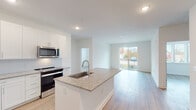 This single-floor unit at The Statesman presents a clean, contemporary design defined by an open-concept layout and a consistent neutral palette throughout. Light hardwood flooring flows seamlessly from the kitchen into the living area, creating a cohesive and airy feel across the main living space.

The kitchen is well-appointed with white shaker-style cabinetry extending to the ceiling, granite countertops, a subway tile backsplash, and a full suite of stainless steel appliances including a refrigerator, electric range, and over-the-range microwave. A central island with an integrated sink and matching granite surface provides additional workspace and casual seating potential. The living area opens directly to a balcony through a large sliding glass door, allowing generous natural light and outdoor views.

The bedrooms are bright and simply finished, each featuring light hardwood floors, white horizontal blinds, and ample natural light from multiple windows. One bedroom includes a ceiling fan. A walk-in closet with wire shelving provides organized storage.

The bathroom features a dual-sink vanity with granite countertops, white cabinetry, a large mirror with contemporary strip lighting, and a tub-shower combination with white tile surround, maintaining the unit's clean, modern aesthetic throughout.