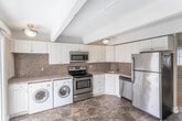 Located in Toms River, NJ, this two-floor home offers a thoughtfully designed layout with a blend of practical finishes and comfortable living spaces throughout. The kitchen is well-equipped with white cabinetry, granite countertops, a mosaic tile backsplash, and a full suite of stainless steel appliances, including a refrigerator, electric range, microwave, and dishwasher — all set atop rich, dark tile flooring that extends into the dining and living areas. The main living space is bright and open, featuring exposed ceiling beams, elegant wainscoting along the walls, and sliding glass doors that flood the room with natural light and provide direct access to an outdoor patio overlooking a spacious green landscape. A decorative front entryway with an ornate staircase connects the two floors. The upper level hosts carpeted bedrooms with vaulted ceilings, ample natural light from large windows, and a relaxed, airy ambiance. Two bathrooms serve the home, each finished with dark tile flooring, white vanities, and clean, understated fixtures. Baseboard heating is present throughout, ensuring year-round comfort. The overall aesthetic is warm and neutral, offering a welcoming and functional environment in a desirable New Jersey location.