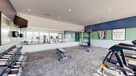 This fitness center offers a comprehensive workout environment designed to support a wide range of exercise routines. The space is finished with durable, patterned carpet tiles and features a crisp white ceiling with recessed lighting that evenly illuminates the entire floor. A striking two-tone accent wall in navy blue and sage green adds energy and visual depth to the room, complemented by framed motivational artwork throughout.

A full-length mirror wall runs along one side, visually expanding the space and providing exercisers with form feedback during workouts. Large windows along the opposite wall flood the room with natural light and offer views of an outdoor pool area and surrounding amenities, creating a bright and inviting atmosphere.

The fitness center is equipped with a variety of cardio machines, including treadmills and ellipticals, arranged to take advantage of the natural light and views. A cable resistance machine anchors the strength training area, accompanied by an adjustable weight bench and a rack of dumbbells catering to various fitness levels. A stationary cycle rounds out the cardio offerings. The open layout provides ample floor space for stretching or bodyweight exercises. Overall, the fitness center delivers a well-organized, motivating environment suited for a complete and effective workout experience.