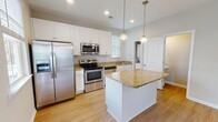 Located in Myrtle Beach, SC, this two-story home offers a thoughtfully designed layout with quality finishes throughout. The kitchen serves as a central highlight, featuring crisp white shaker cabinetry, granite countertops, a central island with pendant lighting, and a full suite of stainless steel appliances including a French door refrigerator, electric range, built-in microwave, and dishwasher. Light hardwood-style flooring runs through the main living areas, complemented by recessed lighting and natural light from multiple windows. The bedrooms are carpeted for comfort and include ceiling fans and generous closet space. The primary bedroom features a tray ceiling and an en-suite bathroom with a walk-in shower, granite vanity, and white cabinetry. A second full bathroom is also finished with granite countertops and includes a tub-shower combination. Additional living spaces on the main floor offer open, airy layouts with neutral tones and hardwood-style flooring, creating a versatile and welcoming environment. The overall aesthetic is clean and contemporary, making this Myrtle Beach home a well-rounded and functional residence.