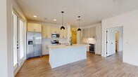 This well-appointed 2-bedroom, 2-bathroom single-story residence offers a thoughtfully designed layout with contemporary finishes throughout. The open-concept kitchen and living area serves as the heart of the home, featuring light wood cabinetry with matte black hardware, a large center island with a white quartz countertop and undermount sink, stainless steel appliances including a French door refrigerator and range, a built-in wine cooler, and a herringbone tile backsplash. Pendant lighting accents the island, while recessed ceiling lights illuminate the full space. Light-toned hardwood flooring flows seamlessly throughout every room. The living area is bright and airy, with multiple windows fitted with blinds that invite generous natural light and outdoor views. Both bedrooms are spacious and comfortable, each featuring ceiling fans and large windows. The primary bathroom is elegantly appointed with a dual-sink vanity, light wood cabinetry, matte black fixtures, framed mirrors, and a glass-enclosed walk-in shower. A generous walk-in closet with built-in shelving and hanging rods provides ample storage. The second bathroom offers a full tub-shower combination with marble-style tile surround, a single-sink vanity, and matching matte black hardware. Clean white walls and consistent finishes create a cohesive, modern ambiance throughout.
